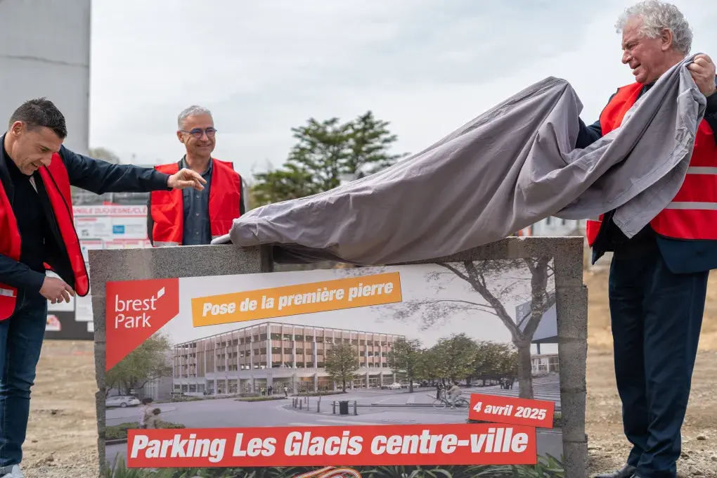 Trois hommes lèvent un voile sur un mur en pierres.