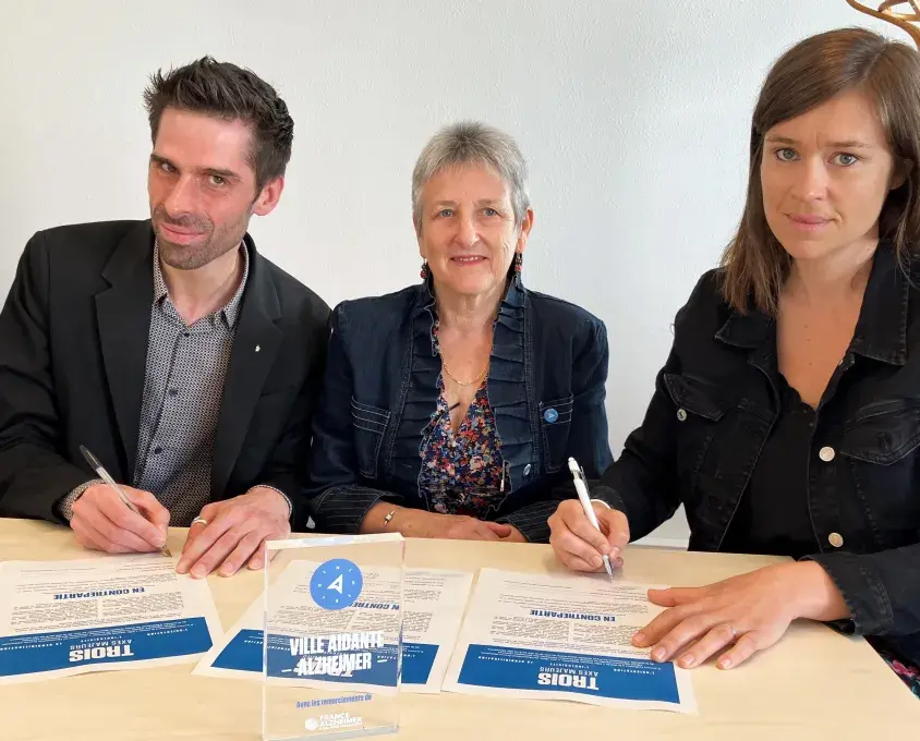 Un homme et deux femmes signent une charte d'engagement. 