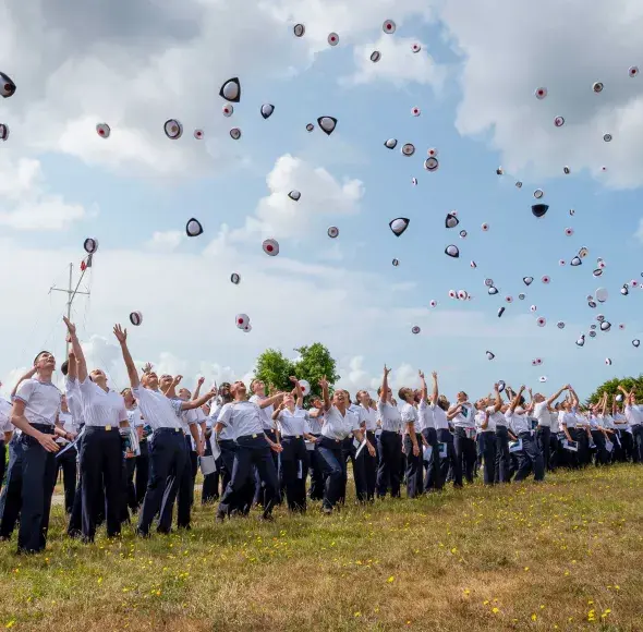 Des hommes et des femmes en uniforme lançant leur couvre-chef en l'air