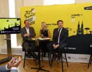 Trois personnes posent devant une affiche.