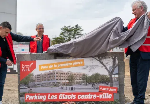 Trois hommes lèvent un voile sur un mur en pierres. 