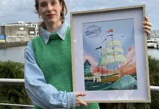 Une femme debout tient un cadre avec l'affiche des Fêtes maritimes de Brest 2027.